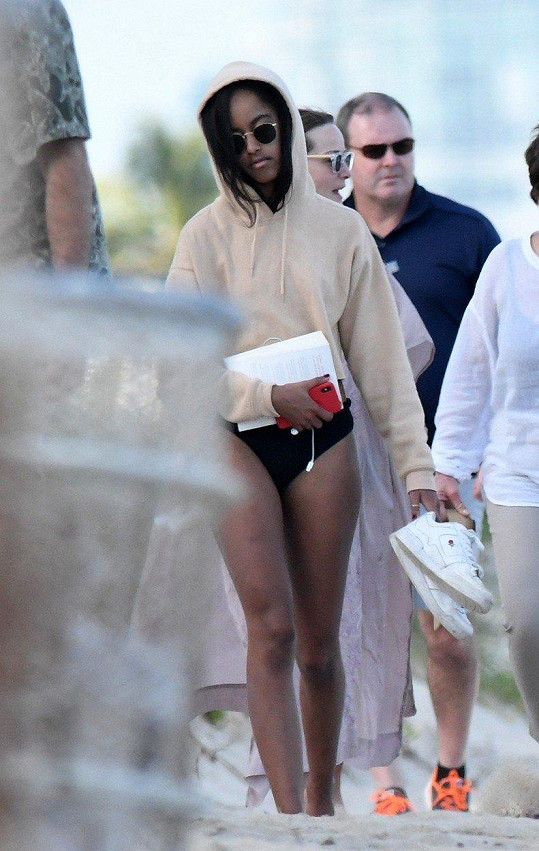 A vedle máti kráčí v plavkách a mikině s kapucí exprezidentova dcera Malia Obama (19).